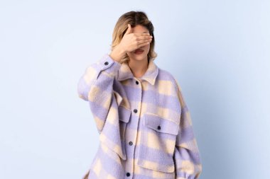 Genç Rus kadın mavi arka planda tek başına, gözleri elle kapatıyor. Bir şey görmek istemiyorum.