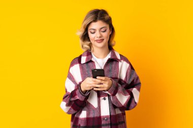 Sarı arka planda izole edilmiş genç bir Rus kadın cep telefonuyla mesaj gönderiyor.
