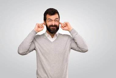 Yakışıklı adam hayal kırıklığına uğramış ve gri arka planda kulaklarını kapatmış.