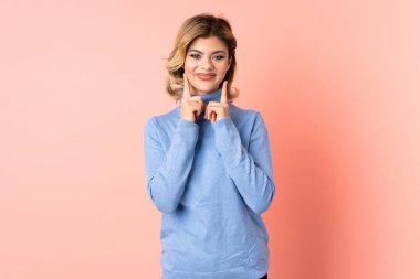 Pembe arka planda izole edilmiş genç Rus kadın mutlu ve hoş bir ifadeyle gülümsüyor.