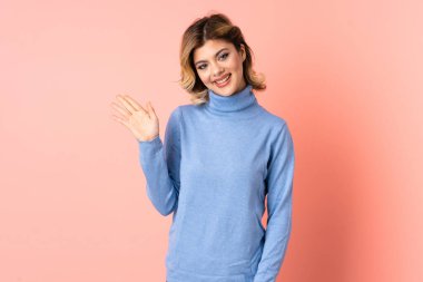 Pembe arka planda izole edilmiş genç Rus kadın mutlu bir ifadeyle selamlıyor.