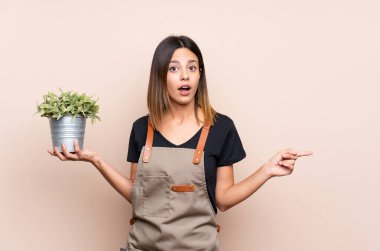 Elinde bir bitki tutan genç kadın şaşırmış ve işaret ediyor.