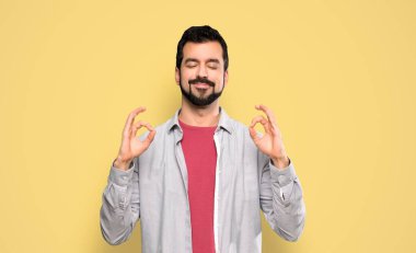 Zen sakallı yakışıklı adam, izole edilmiş sarı arka planda poz veriyor.