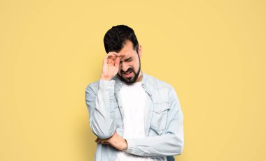 Handsome man with beard with tired and sick expression over isolated yellow background
