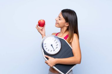 Tartı makinesi ile izole edilmiş mavi arka plan üzerinde tartı makinesi ve bir elma ile kız