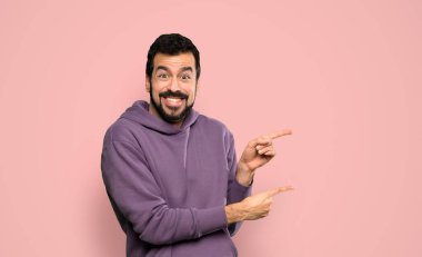 Eşofmanlı yakışıklı adam korkmuş ve pembe arka plan üzerinde yan tarafı işaret ediyor.