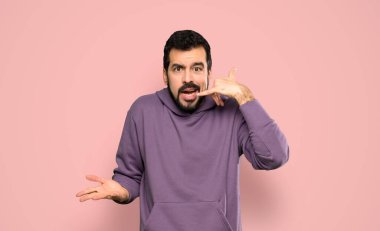 Sweatshirt 'lü yakışıklı adam telefon jesti yapıyor ve izole edilmiş pembe arka plandan şüphe ediyor.