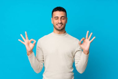 Zen pozisyonunda soyutlanmış mavi arka planı olan genç bir adam