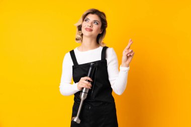 El blenderi kullanan kız sarı arka planda izole edilmiş ve şans diliyor.