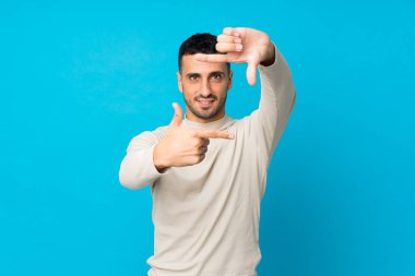 İzole edilmiş mavi arka planda odaklanan genç bir adam. Çerçeve sembolü