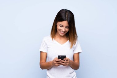 İzole edilmiş mavi arka plan üzerinde genç bir kadın cep telefonuyla bir mesaj ya da e-posta gönderiyor