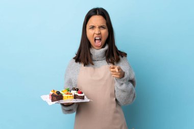 Pasta şefi elinde büyük bir pasta tutuyor mavi arka planda hayal kırıklığına uğramış ve ön tarafı işaret ediyor..