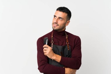 Kuaför ya da berber elbisesi ve elinde saç kesme makinesi olan izole edilmiş beyaz bir geçmişi olan genç adam.