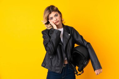 Sarı arka planda izole edilmiş motosiklet kaskı taşıyan genç bir kadın mutsuz ve hayal kırıklığına uğramış.