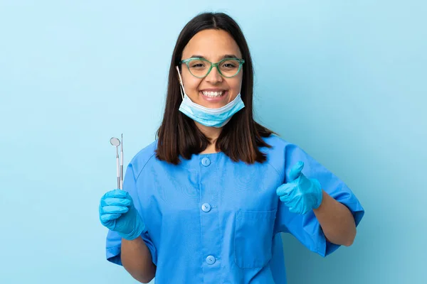 年轻的黑发混血女牙医拿着工具在孤立的背景上拿着手心想象的复制空间插入广告并竖起大拇指 — 图库照片