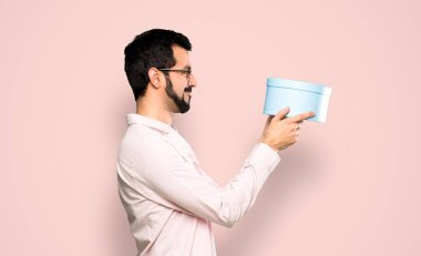 Handsome man with beard holding a gift over isolated pink background