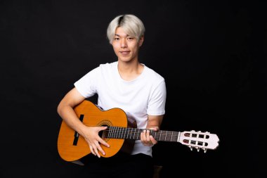 Siyah arka planda gitar çalan Asyalı genç adam çok gülümsüyor.