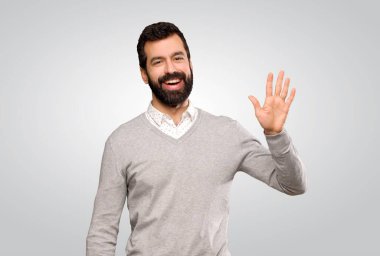 Gri arka planda mutlu bir ifadeyle selamlayan yakışıklı bir adam.