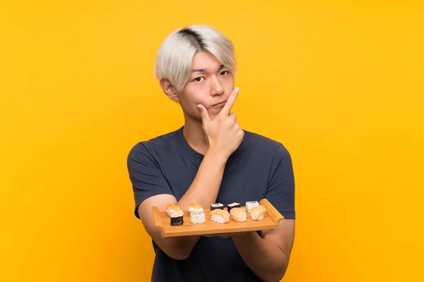 Mladý Asijský Muž Sushi Přes Izolované Žluté Pozadí Myšlení Nápad — Stock fotografie