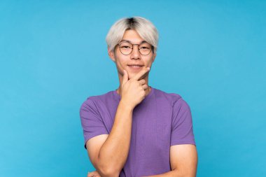 Gözlüklü ve gülümseyen, soyutlanmış mavi bir geçmişi olan Asyalı genç bir adam.