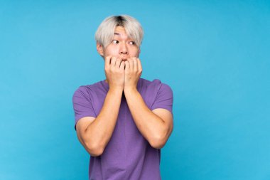 Asyalı genç adam izole edilmiş mavi arka planda gergin ve korkmuş bir şekilde elleriyle suni teneffüs yapıyor.