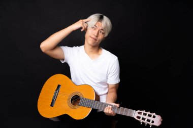 Siyah arka planda gitar çalan Asyalı genç adamın şüpheleri ve kafası karışmış bir ifadesi var.
