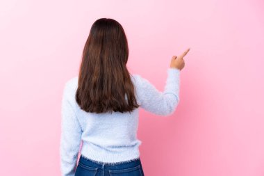 İzole edilmiş pembe arka planı olan genç Kolombiyalı kız işaret parmağıyla işaret ediyor.