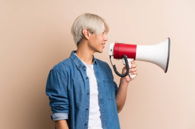 Asyalı genç bir adam izole edilmiş arka planda megafondan bağırıyor.