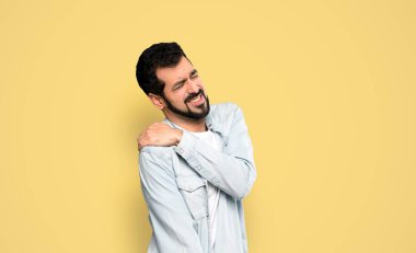 Omzunda ağrıdan muzdarip sakallı yakışıklı adam izole edilmiş sarı arka plan üzerinde çaba sarf etmiş.