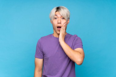 Asyalı genç adam mavi arka planda, şaşırmış ve şok olmuş bir yüz ifadesi var.