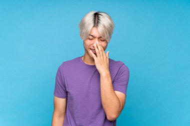 Soyutlanmış mavi arka planda genç Asyalı adam çok fazla gülümsüyor.