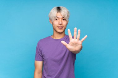 Asyalı genç adam izole edilmiş mavi arka planda beş parmaklı sayıyor.
