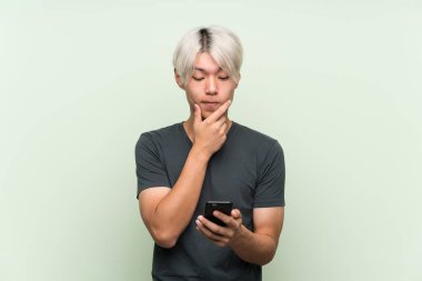 Asyalı genç adam yeşil arka planda düşünüyor ve bir mesaj gönderiyor.