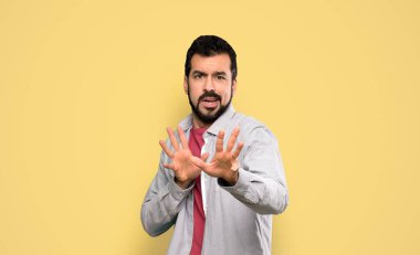 Yakışıklı, sakallı, gergin, elini öne uzatan, izole edilmiş sarı arka planı olan adam.