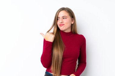 Genç sarışın kız izole edilmiş beyaz arka planda mutsuz ve kenarı işaret ediyor.