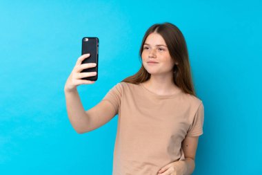 İzole edilmiş mavi arka planda Ukraynalı genç kız selfie çekiyor.