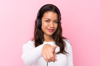 İzole edilmiş pembe duvarın üstünde kulaklıkları olan genç bir kadın.