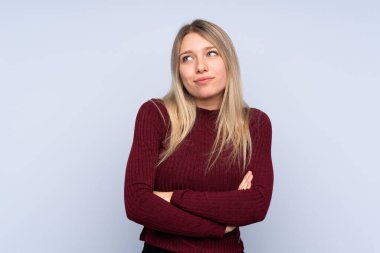 Soyutlanmış mavi arka planda genç sarışın kadın, omuzlarını kaldırırken şüpheli hareketler yapıyor.