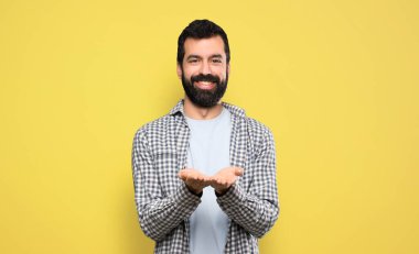 Handsome man with beard holding copyspace imaginary on the palm to insert an ad