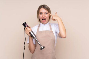 Genç sarışın kadın el blenderi kullanıyor. Çözümü bulmaya çalışıyor.