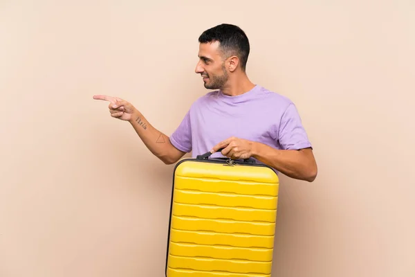 商品を提示するために側面を指して隔離された背景の上にスーツケースを保持している男 — ストック写真