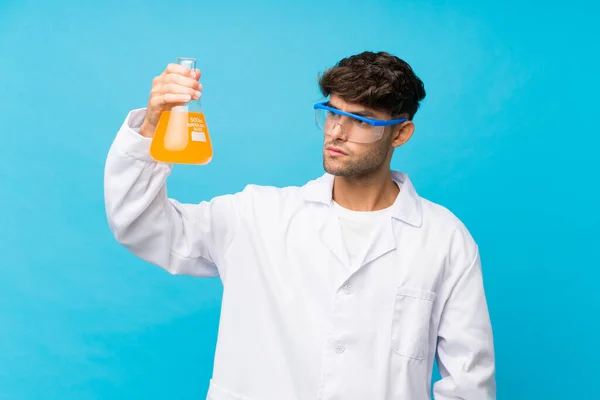 Joven Hombre Guapo Sobre Fondo Azul Aislado Con Tubo Ensayo —  Fotos de Stock