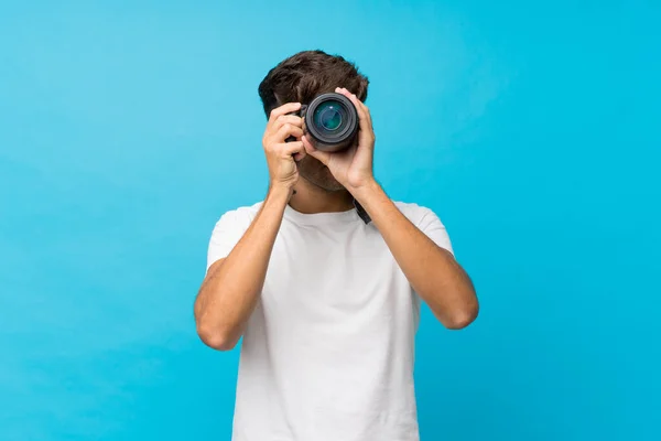 Giovane Bell Uomo Sfondo Blu Isolato Con Una Fotocamera Professionale — Foto Stock
