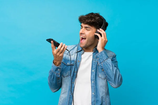 Młody Przystojny Mężczyzna Odizolowanym Niebieskim Tle Pomocą Telefonu Komórkowego Słuchawkami — Zdjęcie stockowe