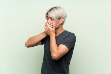 Asyalı genç adam yeşil arka planda, ağzı kapalı ve yana bakıyor.