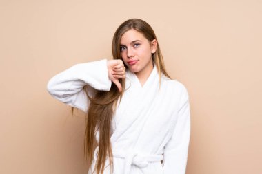 Bornozlu genç bir kız izole bir arka planda baş parmak aşağı işareti gösteriyor.