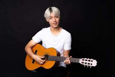 Siyah arka planda gitar çalan Asyalı genç bir adam.