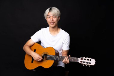 Siyah arka planda gitar çalan Asyalı genç bir adam.