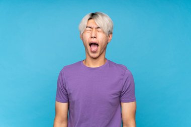 Soyutlanmış mavi arka planda genç bir Asyalı ağzı açık bağırıyor.