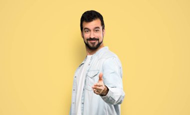 Sakallı yakışıklı adam, izole edilmiş sarı arka planda iyi bir anlaşma için el sıkışıyor.